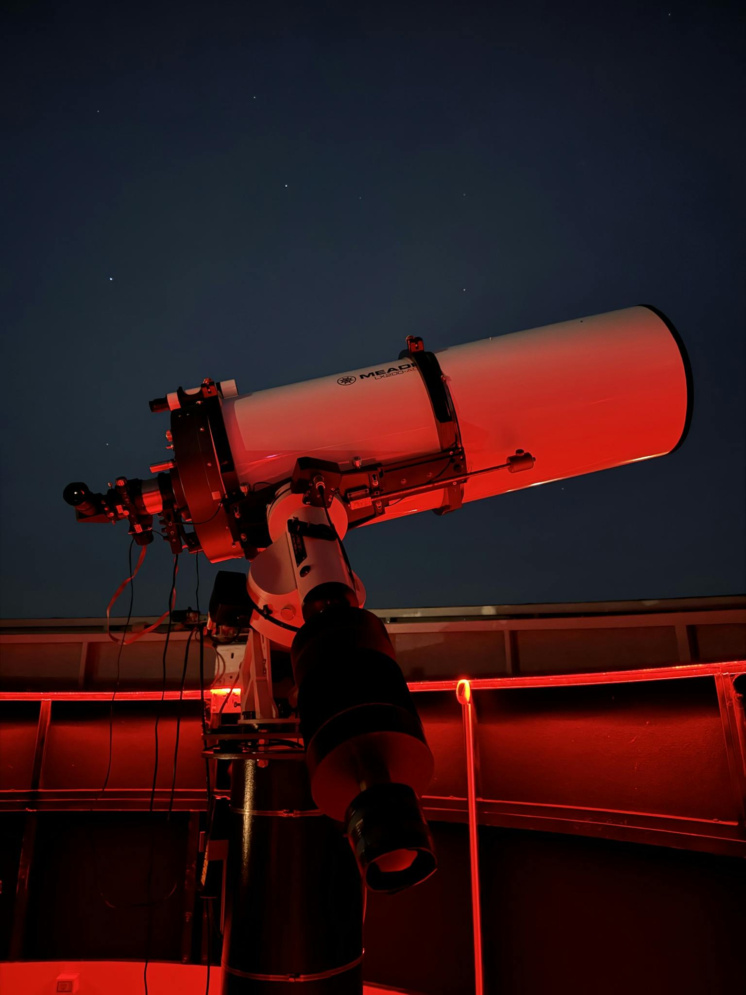 A telescope inside a red-lit observatory pointed at the night sky, capturing celestial views.